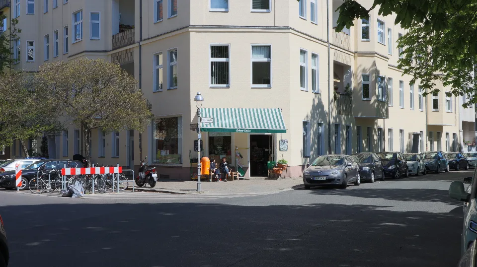 Helles Eckhaus mit grün gestreifter Markise und kleinem Laden.