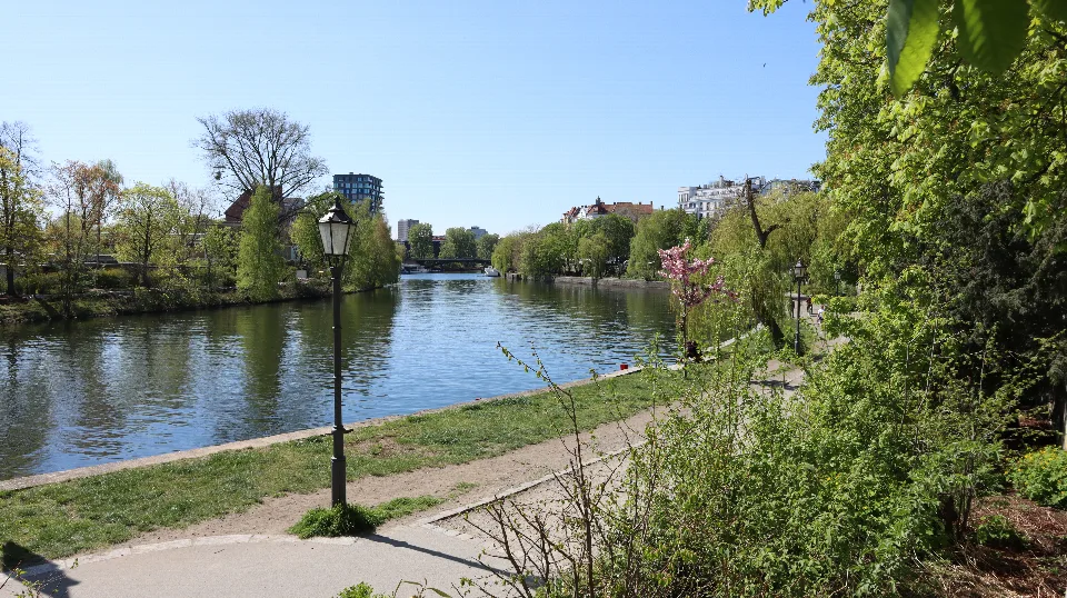 Eine alte Straßenlaterne am Uferweg zwischen Wasser und frischem Grün.