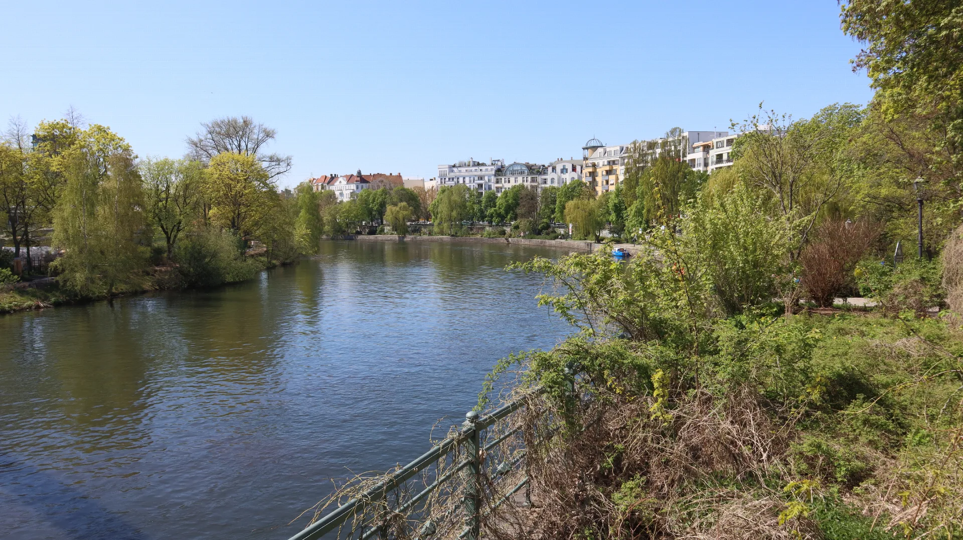Wohnhäuser und frühlingsgrüne Bäume spiegeln sich im Wasser.