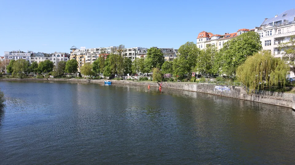 Häuser, Uferpromenade und blühende Bäume auf der anderen Seite des Wassers.